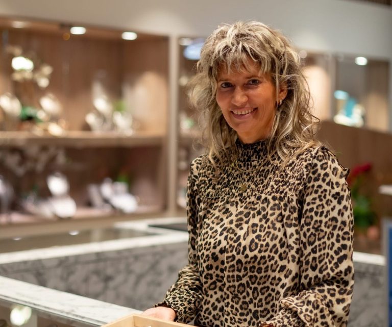 Frau mit lockigem Haar in einem Schmuckgeschäft, trägt ein Leopardenmuster-Oberteil.