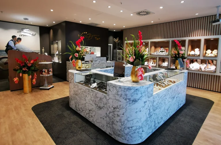 Schmuckgeschäft mit eleganter Theke, Blumenarrangements und Vitrinen voller Schmuckstücke.