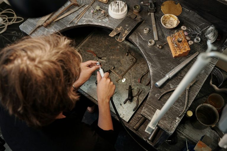Junger Mensch arbeitet an einem Tisch mit Werkzeugen und Materialien für Schmuckreparatur