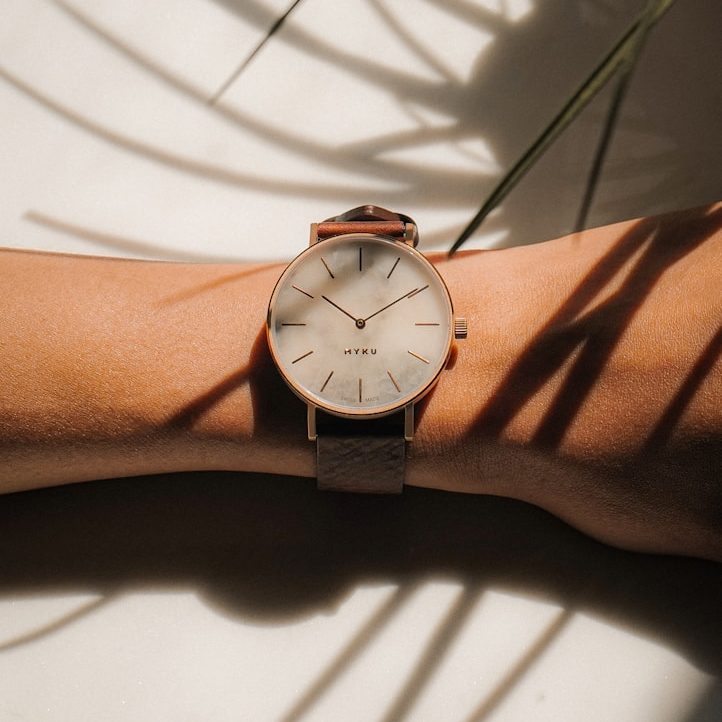 Eine Uhr mit braunem Lederarmband auf einem Handgelenk, umgeben von Schatten.