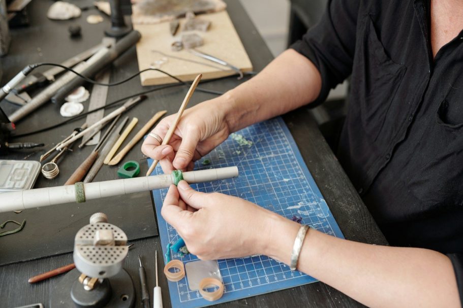 Eine Person arbeitet an einem handwerklichen Projekt mit Werkzeugen und Materialien auf einem Tisch.